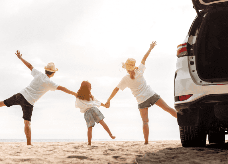 Famiglia felice che corre sulla spiaggia con auto al tramonto.