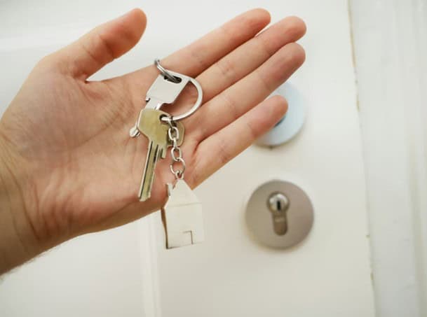 Key to a door with a keychain in hand.