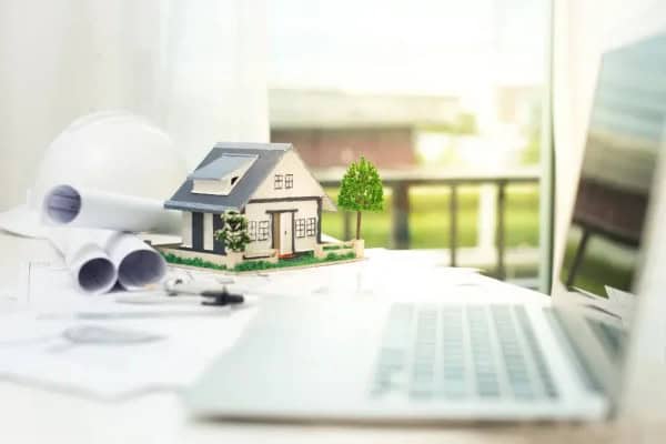 Home maintenance planning with a house model, laptop, and tools on a desk.