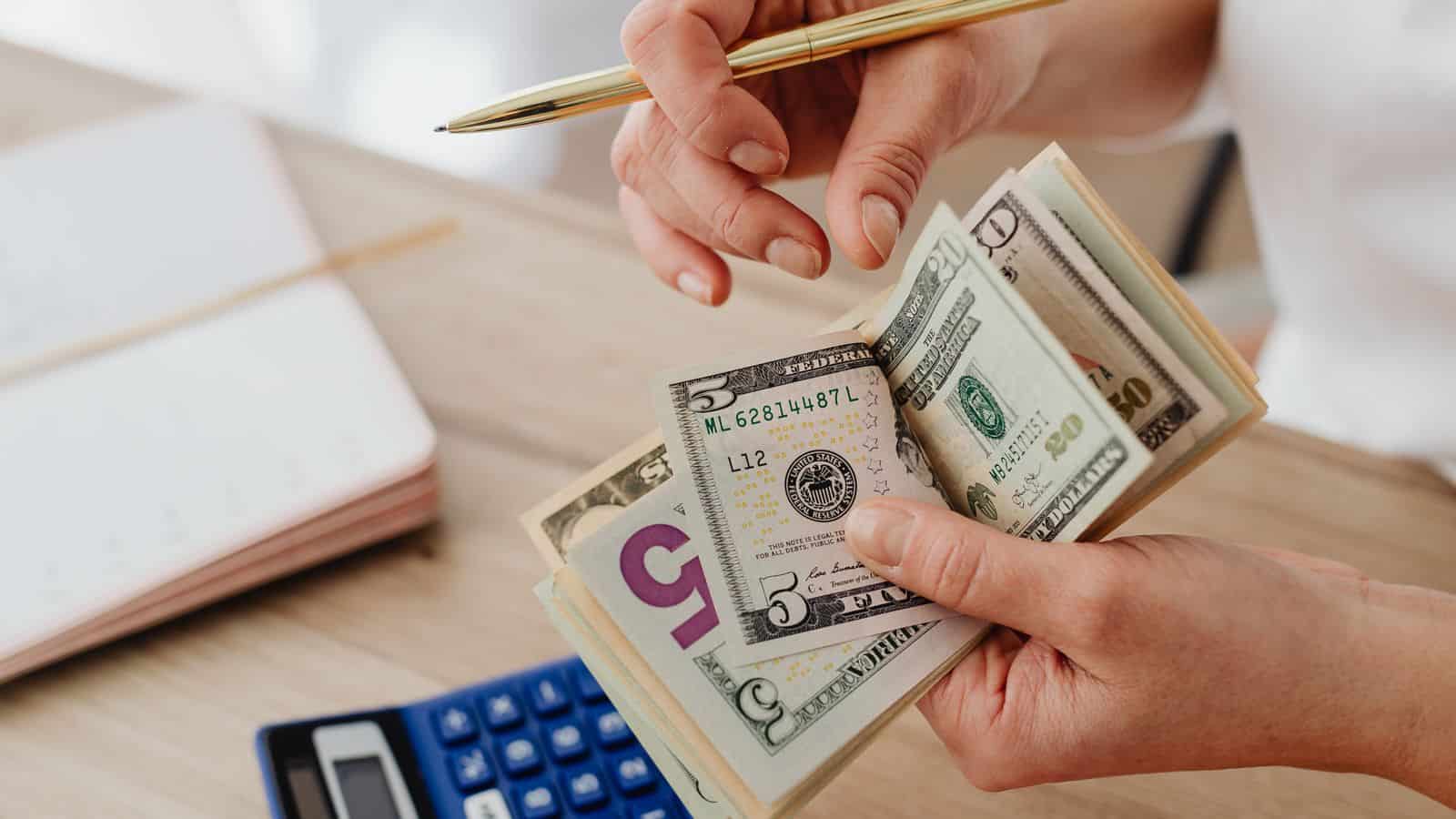 A person counting cash with a calculator and bills while planning a rental budget