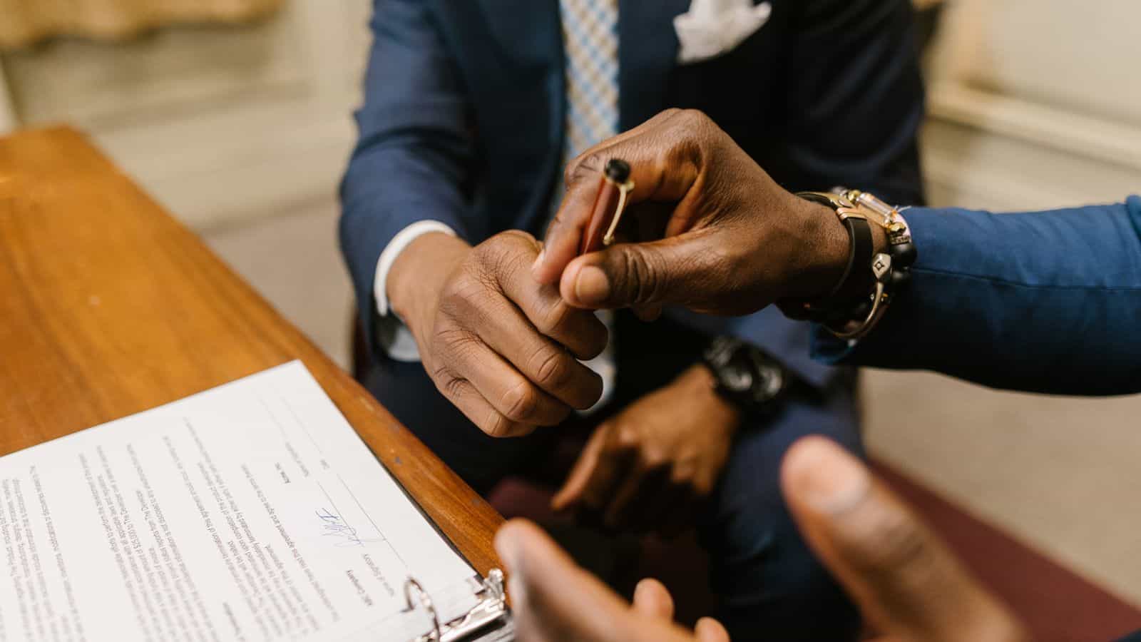A person handing a pen across a desk to sign a rental lease agreement