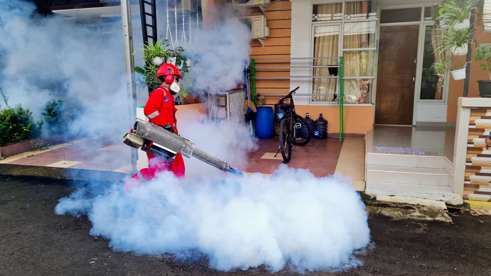 Pest control technician treating the exterior of a home with professional fogging equipment