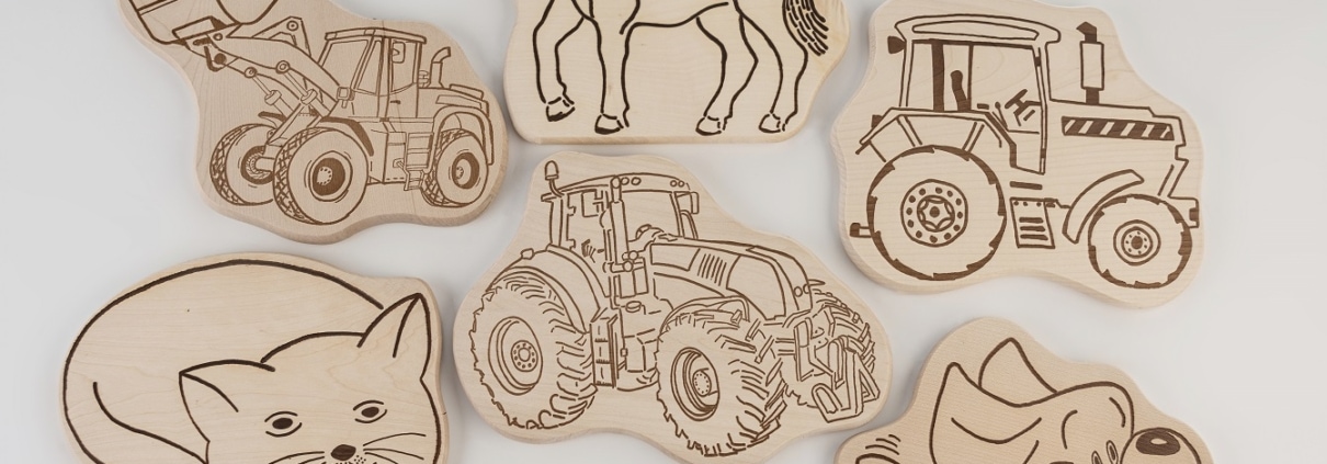 Spielzeug aus Holz, landwirtschaftliche Fahrzeuge und Tiermotive in Holzgravur.