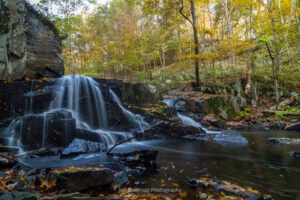 A long exposure photo of Middle Falls on Black Creek in Highland with the trees in the background covered in yellow fall foliage.
