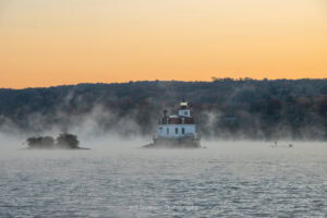 Autumn mist rising up off of the Hudson River at the Esopus Lighthouse as a lone fisherman fishes from a boat on an October morning.