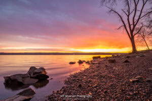 An orange and pink sunrise over the Hudson River from the shoreline of Lighthouse Park.