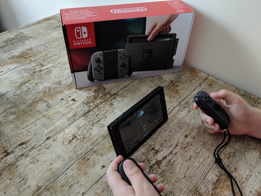 A person using a black Nintendo Switch on wooden surface