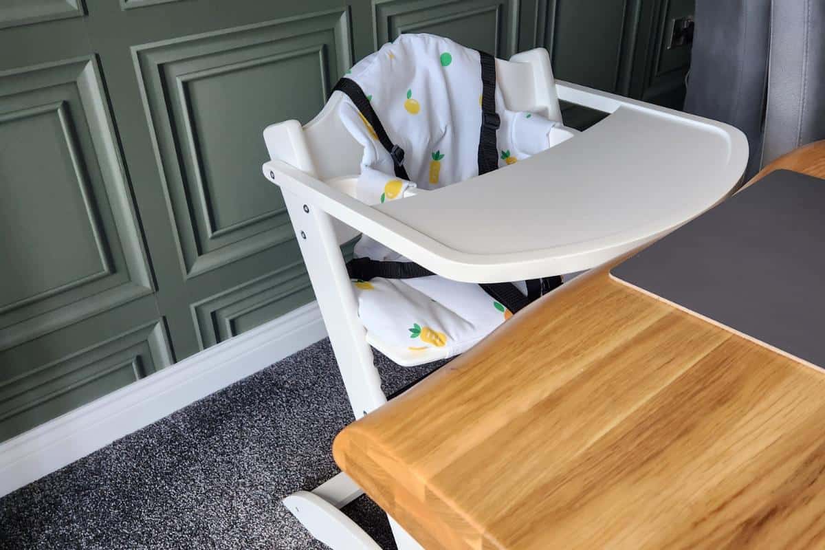 mokee white high chair next to an oak table.