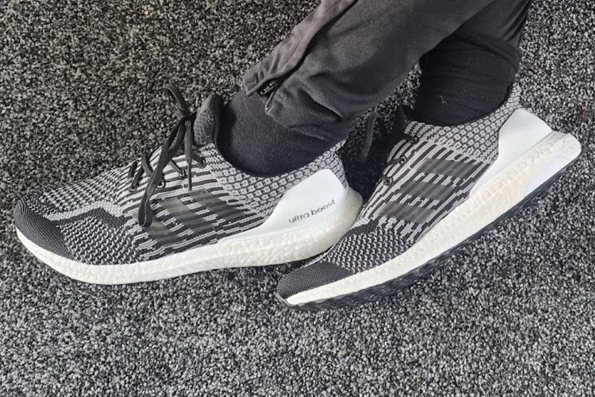 Feet wearing black and white adidas trainers.