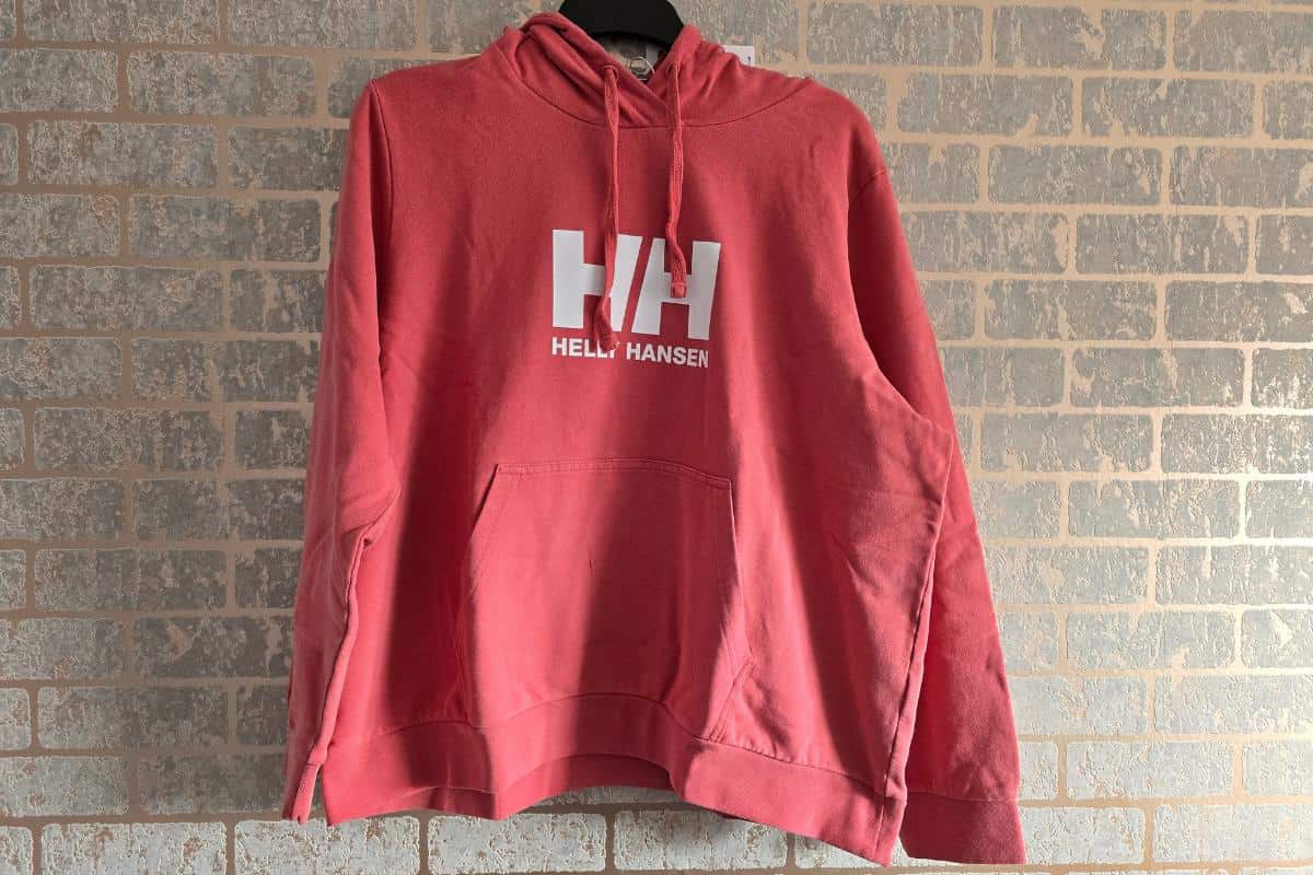 Red hoodie with "Helly Hansen" and "HH" logo on the front, hanging against a brick wall background. Perfect for your Mother’s Day Gift Guide, this stylish option is sure to delight any mum who values comfort and fashion.