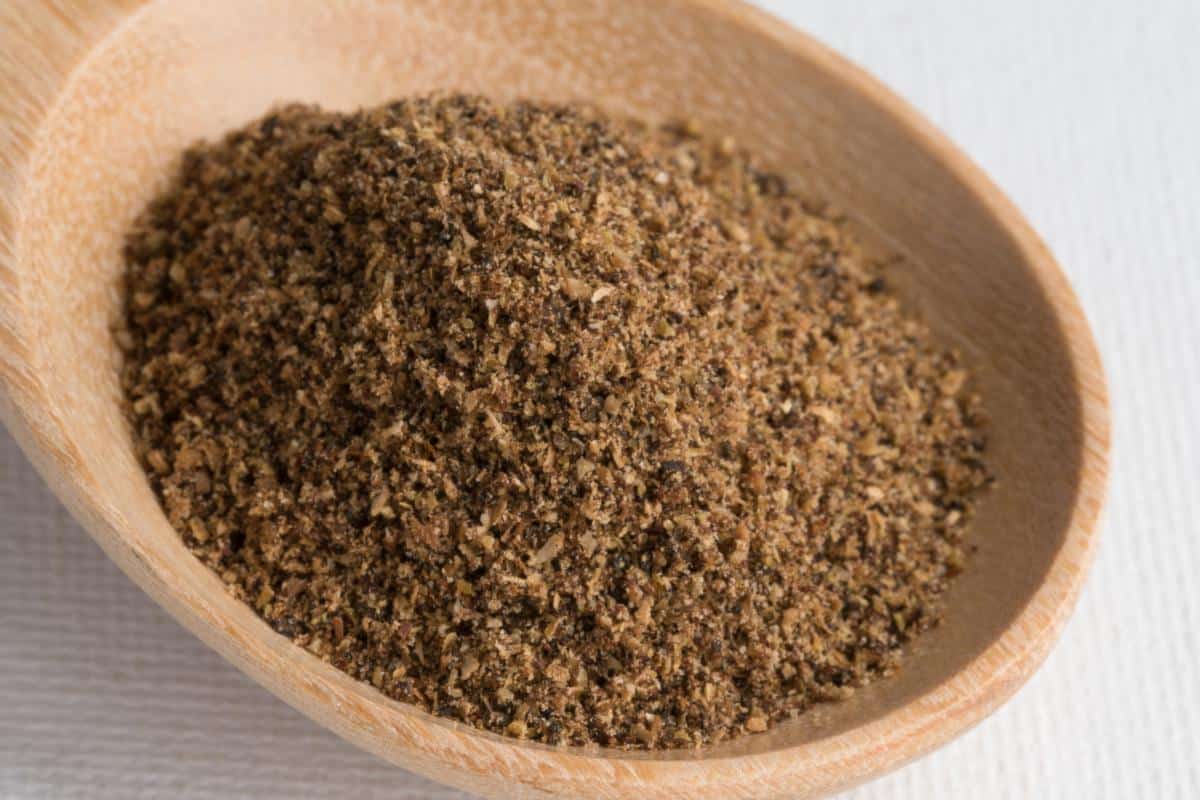 A close-up of a wooden spoon filled with garam masala, a classic warming spice blend often used in family meals, placed on a white textured surface.