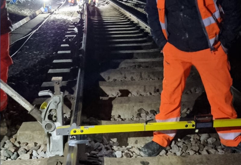 Surveyor standing across rail tracks taking measurements.