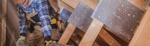 Worker installing metal sheet panels on wooden framework in construction site.