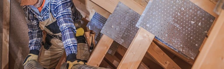 Worker installing metal sheet panels on wooden framework in construction site.