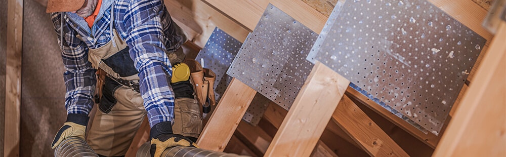 Worker installing metal sheet panels on wooden framework in construction site.