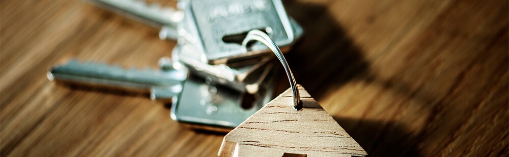 Key on wooden table with house-shaped keychain.