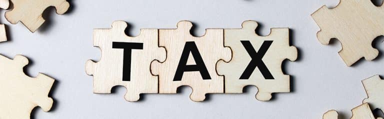 Wooden puzzle pieces spelling "TAX" on a light background.