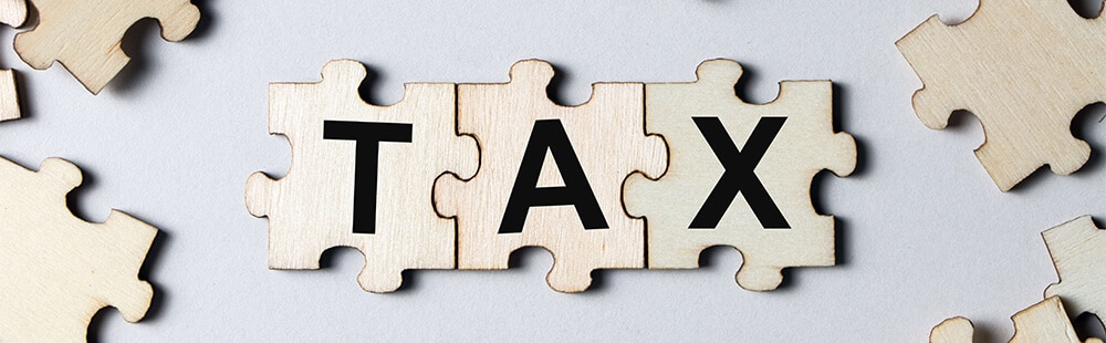 Wooden puzzle pieces spelling "TAX" on a light background.