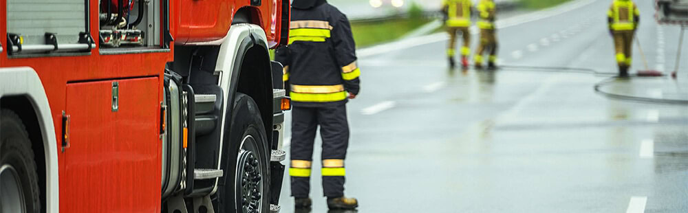 Firefighters in protective gear working near a fire truck on a rainy day.