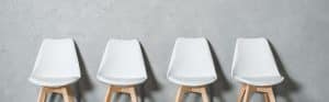 White modern chairs with wooden legs arranged in a row on grey background.