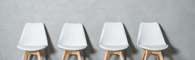 White modern chairs with wooden legs arranged in a row on grey background.