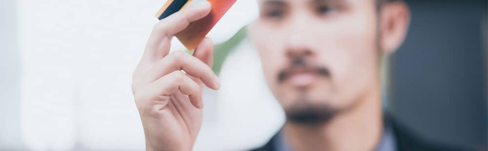 Man holding smartphone for selfie, casual outdoor setting, blurred background.