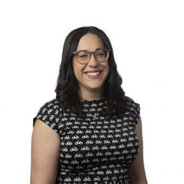 Woman with glasses smiling, wearing a black and white patterned top.
