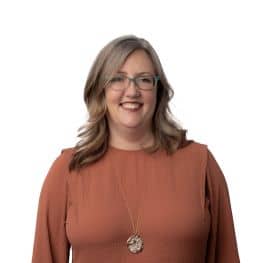 Portrait of a smiling woman with glasses and brown top.