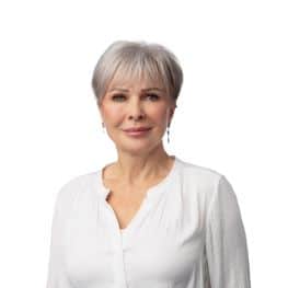 Senior woman with short grey hair, wearing a white blouse, smiling confidently.