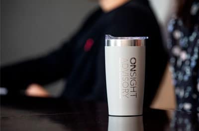 Coffee tumbler with "OnSight Advisory" logo on a dark table, blurred background.