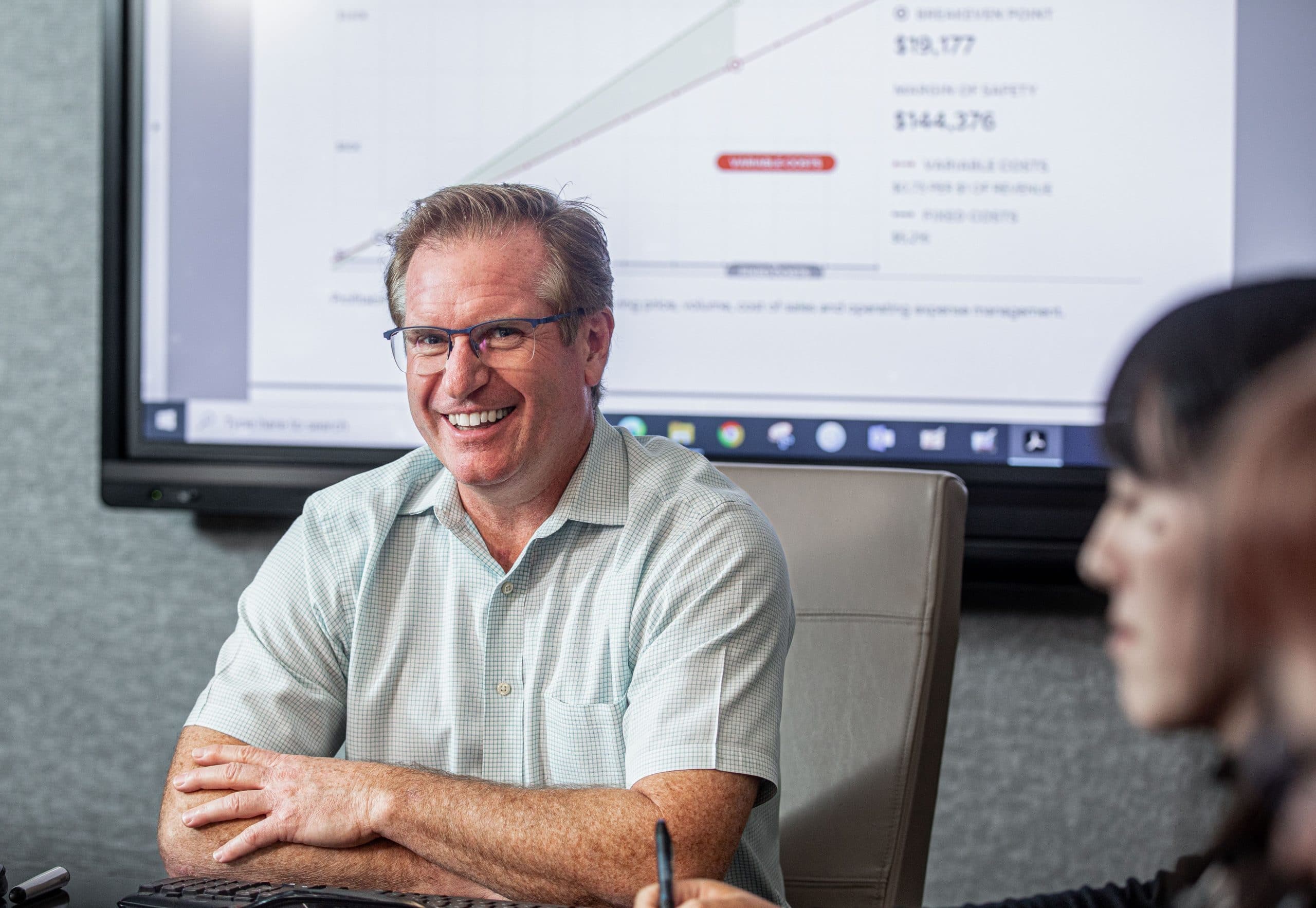 A smiling man in a business meeting, presenting financial data on a large screen during a corporate.