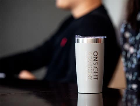Coffee tumbler with "OnSight Advisory" logo on a dark table, blurred background.