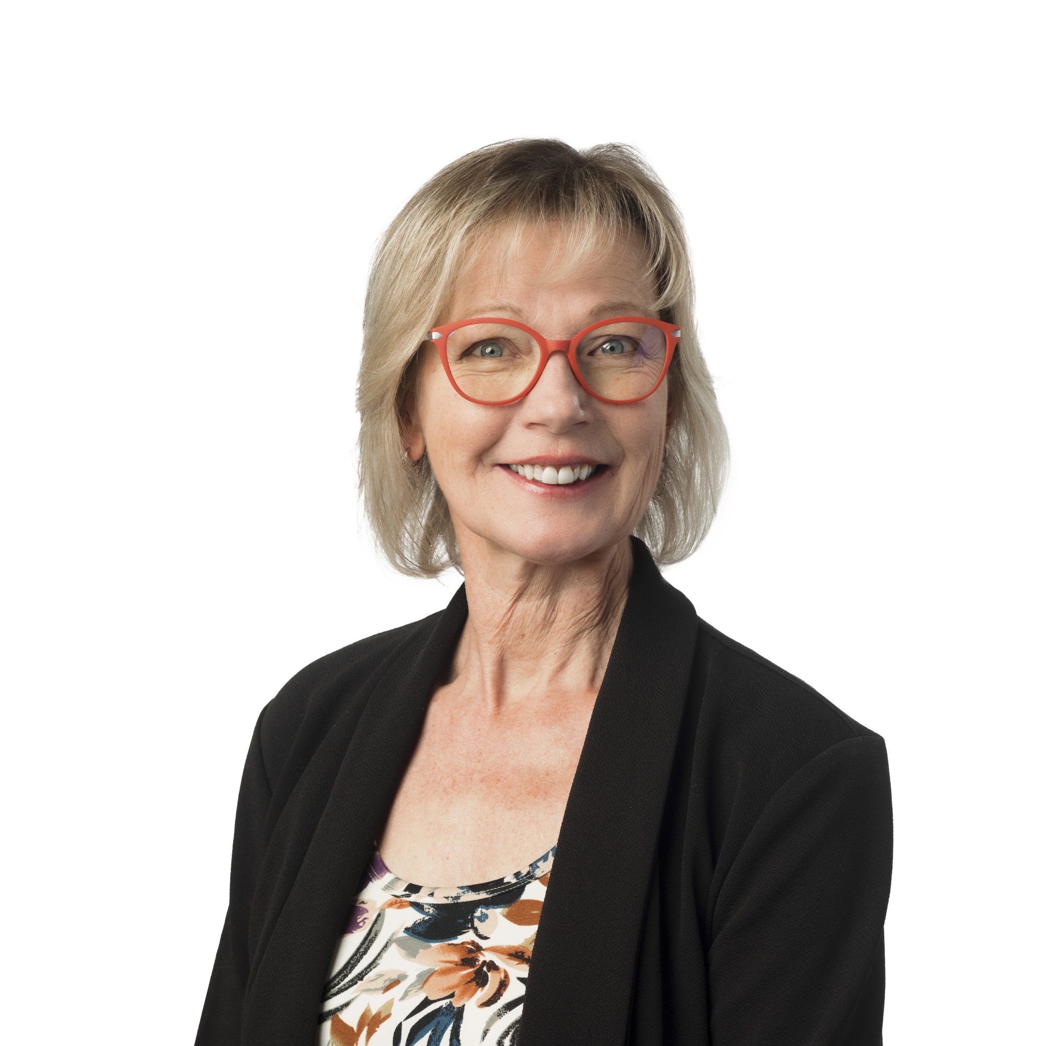 Senior woman with glasses smiling, wearing a black blazer and floral blouse.