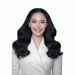 Woman with long, wavy black hair wearing a white blazer, smiling confidently.
