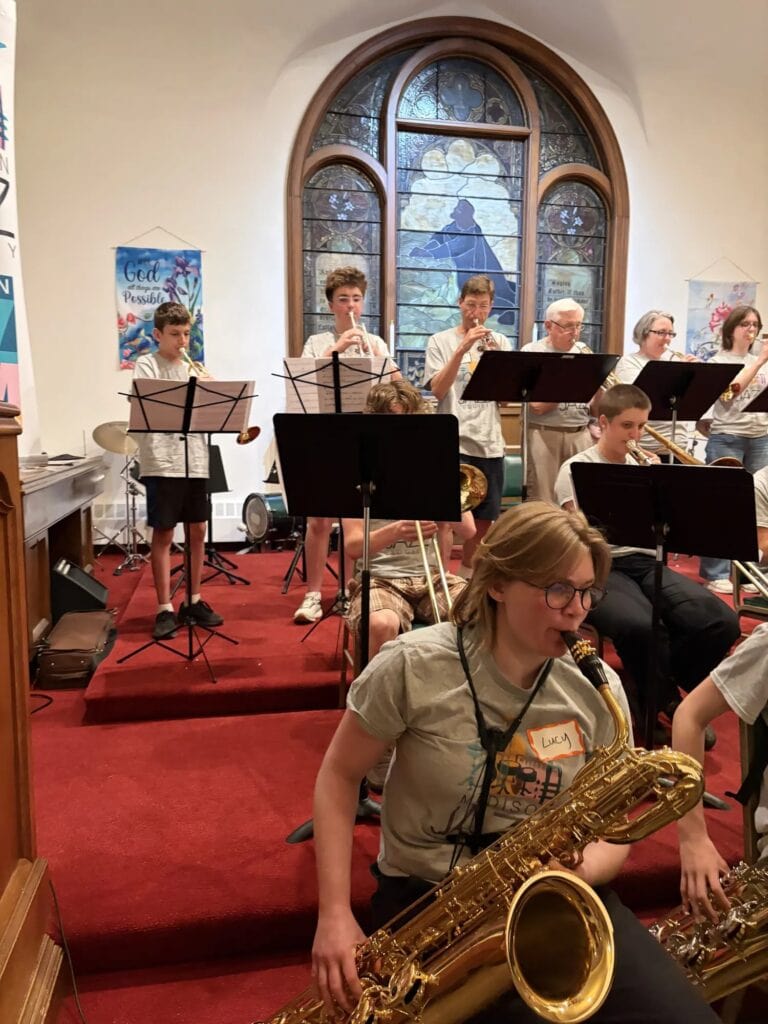 A saxophonist in the foreground as a large ensemble rehearses in the sanctuary at iGnitE jAzz! 2026.