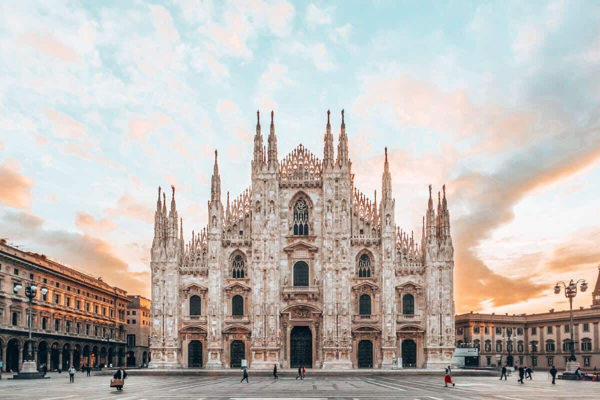 A grand and ornate cathedral on a large square at sunset