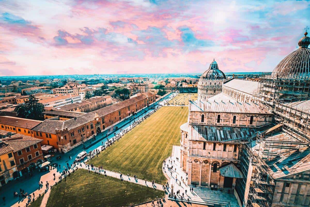A view looking out from the Tower of Pisa across grand buildings and lawns in the Square of Miracles
