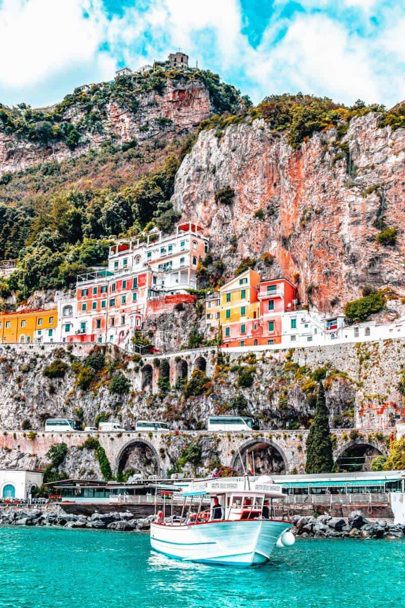 A boat in water in front of a cliff with pretty pastel buildings