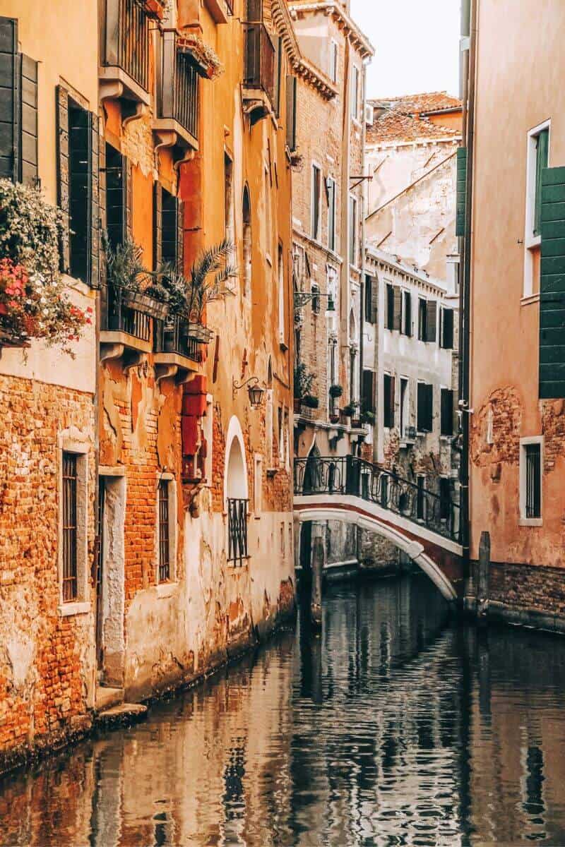 A quaint and quiet canal between tall golden buildings in Venice