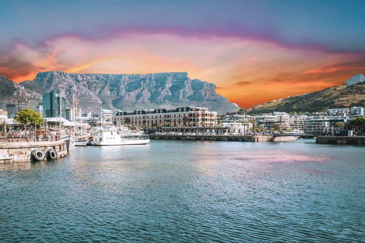 A built up harbour with a backdrop of mountains under a sunset sky