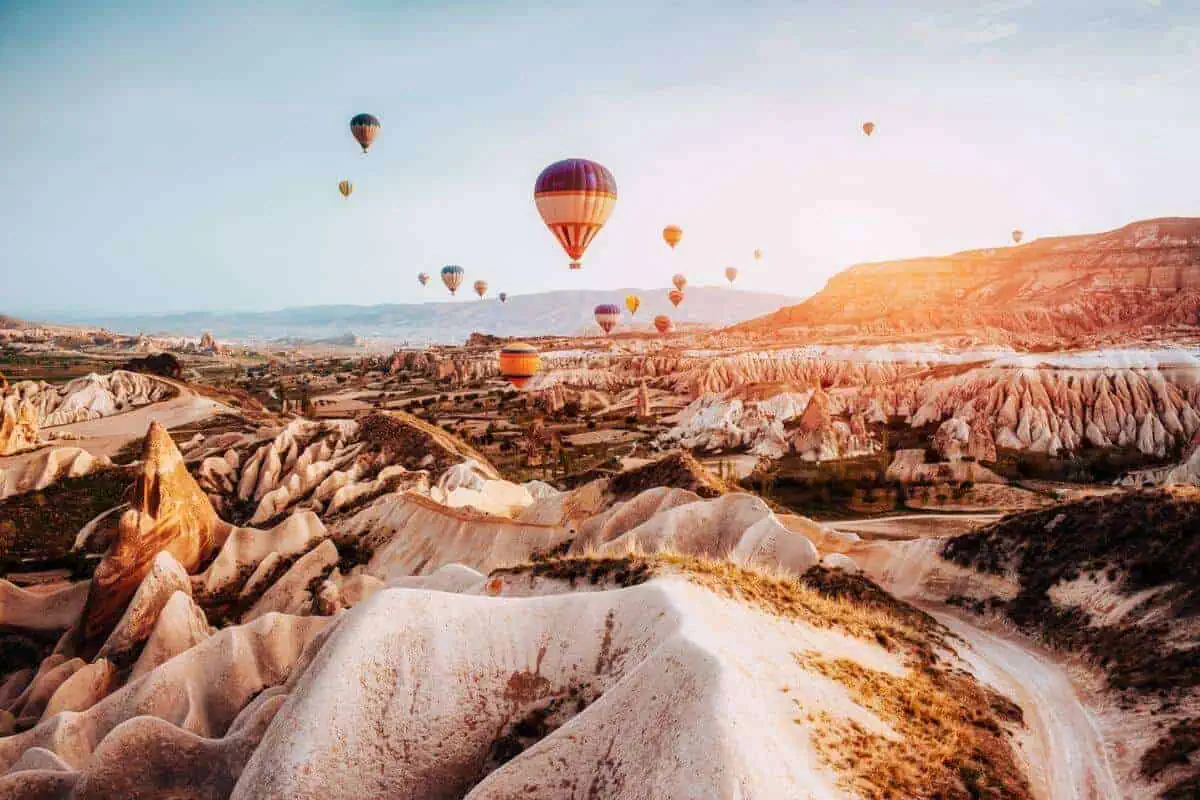 Several multi-coloured hot air balloons above a dramatic rocky landscape