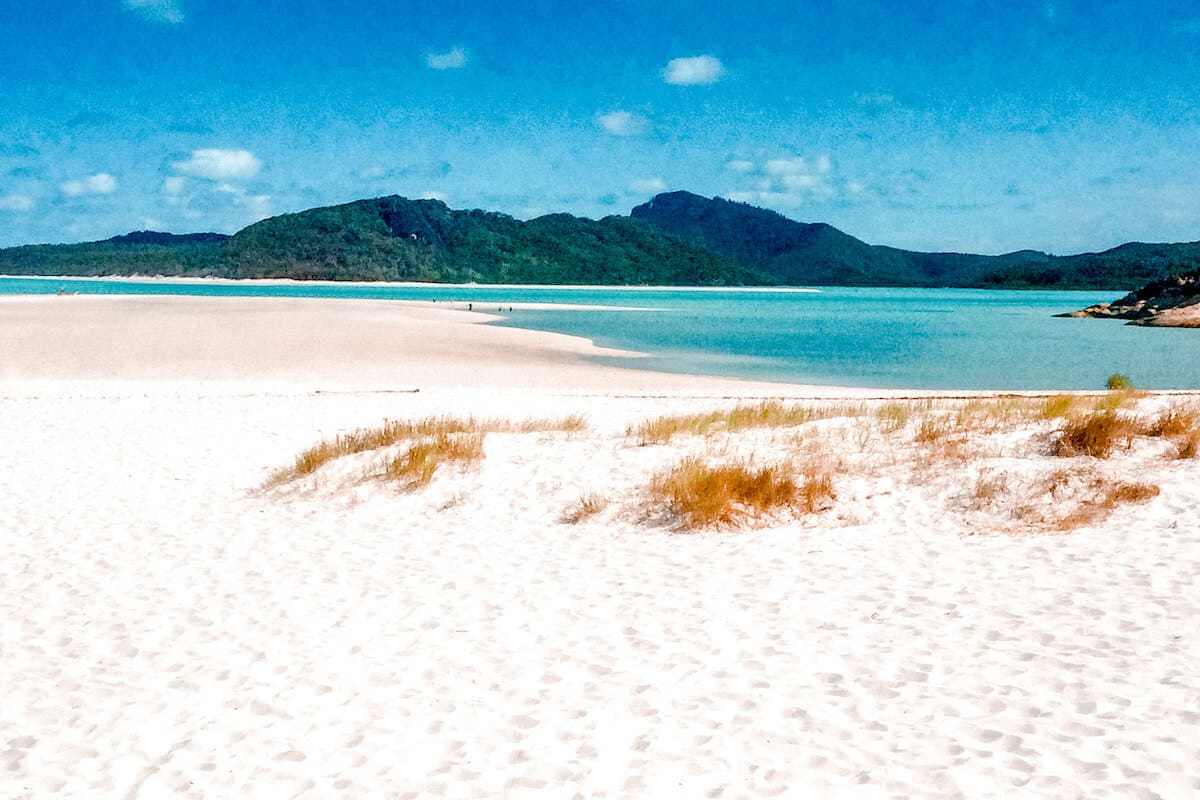 A pristine white-sand beach with turquoise waters and tropical mountains in the background