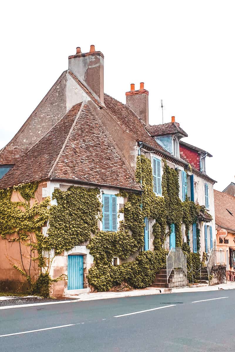 A traditional French building with blue shutters, covered in greenery