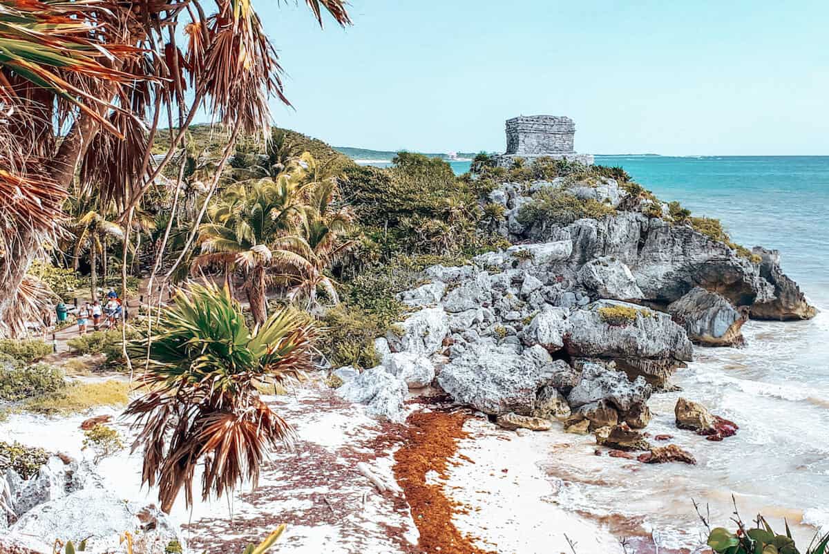 A view across to a Mayan temple ruin on a palm-fringed, beachside clifftop in Tulum