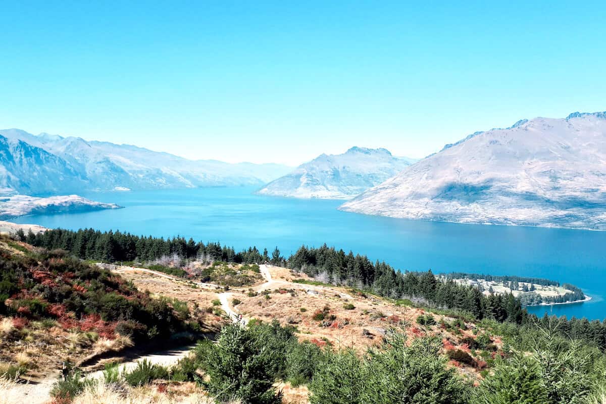 A bright blue lake next to forests and mountains on a clear sunny day in New Zealand