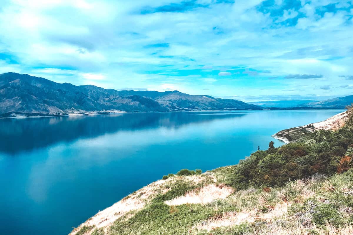 View across a large tranquil lake in New Zealand with a mountain backdrop and blue sky
