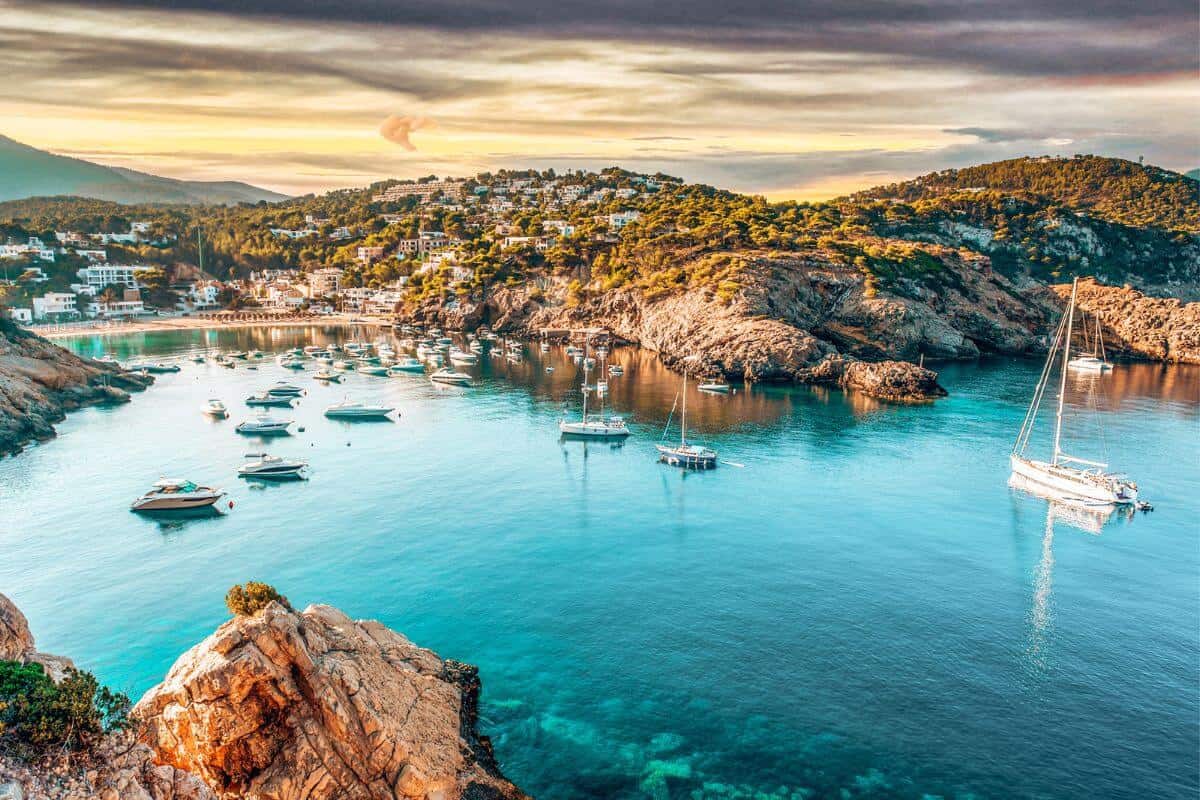 A view across a beautiful, rugged bay in Ibiza with yachts at sunset