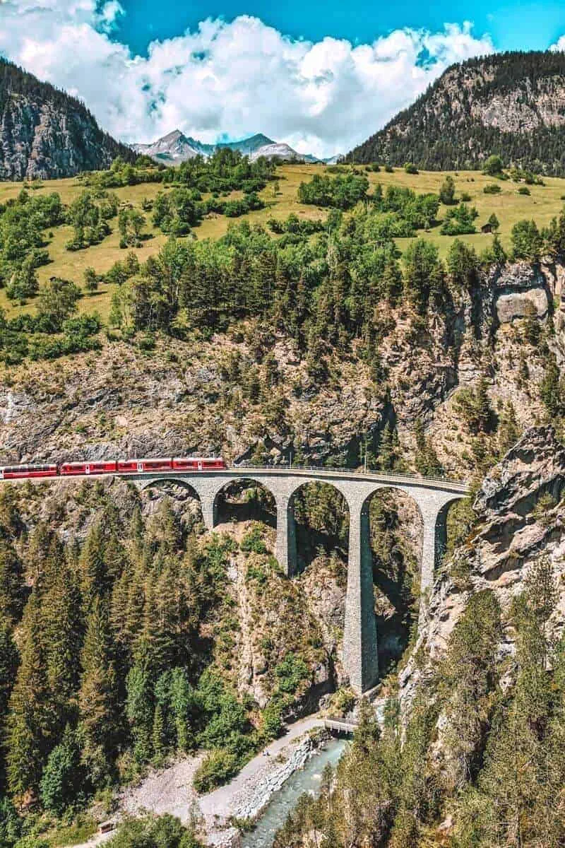 A red train travelling over a viaduct in the mountains in Switzerland