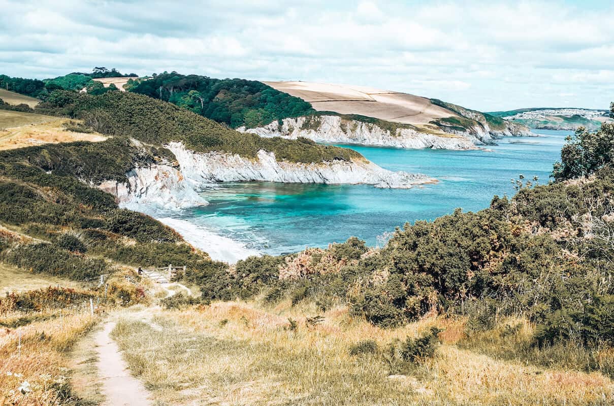 A coastal walking path in Cornwall with views of fields and turquoise sea