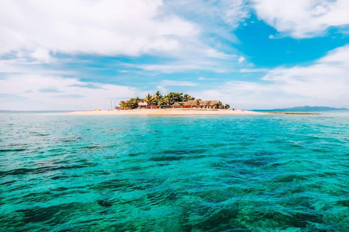 A view across the sea towards a tiny, white-sand tropical island in the Mamanuca region of Fiji